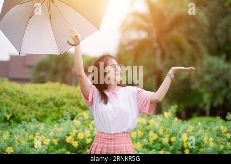 Joyeux adolescent asiatique mignon avec parapluie pretect de la pluie en saison de pluie ou lumière uv du soleil en été Banque D'Images