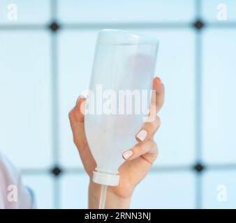 jeune femme tenant une bouteille en plastique avec un médicament intraveineux pour un compte-gouttes dans ses mains Banque D'Images