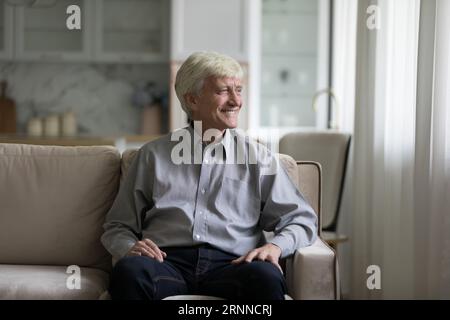 Joyeux homme âgé rêveur regardant la fenêtre loin, souriant Banque D'Images