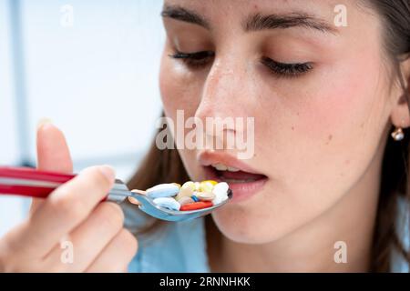 une fille apporte une cuillère remplie de pilules à sa bouche. la notion de médication incontrôlée et de toxicomanie Banque D'Images