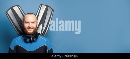 Portrait en gros plan de bel homme de plongée plongeur avec des palmes sur fond bleu de mur de studio Banque D'Images