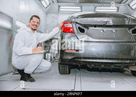 travailleur masculin professionnel de peintre de carrosserie de voiture vérifiant le détail de peinture de couleur dans l'atelier de carrosserie de garage automobile Banque D'Images