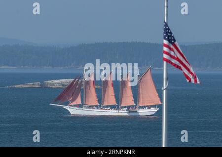 Goélette à quatre mâts en pleine voile, à Bar Harbor avec le drapeau américain au premier plan. Banque D'Images