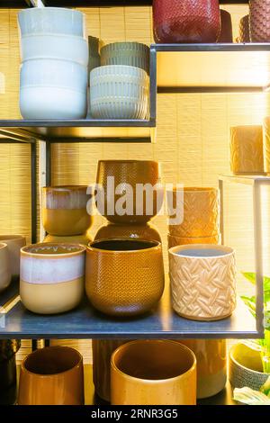 Collection de pots en argile de différentes tailles, couleurs et textures placés soigneusement sur des étagères avec un store en bambou au fond. Banque D'Images