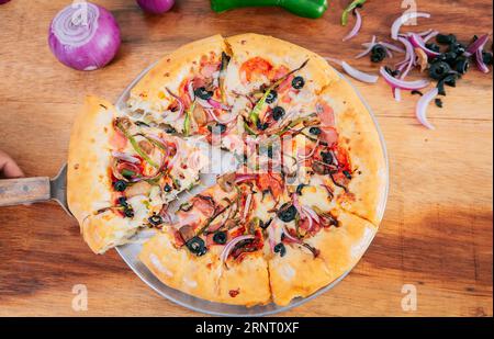 Vue de dessus de spatule prenant une tranche de pizza suprême avec des légumes. Spatule prendre une tranche de pizza suprême avec la spatule, vue à grand angle Banque D'Images