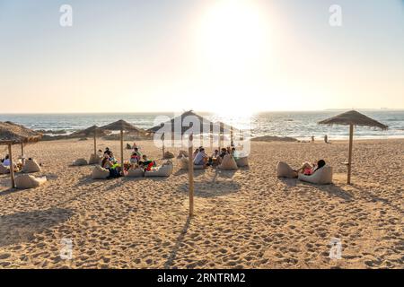 06.22.2023. Porto, Portugal : Bar élégant sur la plage de Porto Portugal avec parasols en roseau et les gens profitant du coucher du soleil Banque D'Images