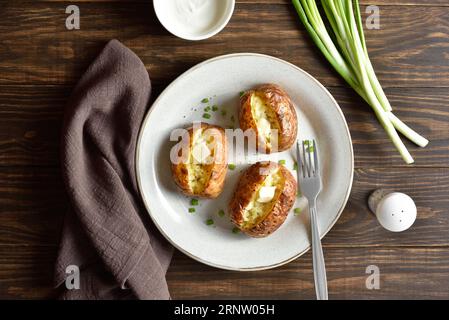 Pomme de terre cuite au four avec beurre et oignon vert sur plaque sur fond de bois. Vue de dessus, pose à plat Banque D'Images