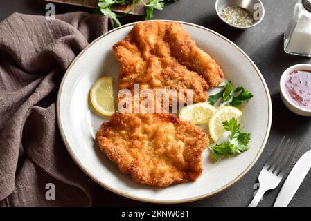 Schnitzel avec citron et feuilles de persil sur plaque blanche sur fond de pierre marron. Gros plan Banque D'Images