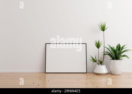 Maquette de cadre photo horizontal noir sur un mur blanc pièce vide avec des plantes sur un plancher en bois Banque D'Images