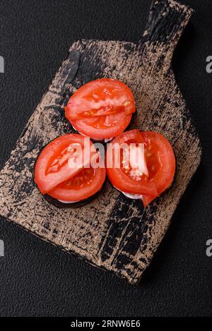 Délicieuse aubergine coupée en cercles grillée et cuite avec de la mayonnaise et des tomates sur un fond de béton foncé Banque D'Images