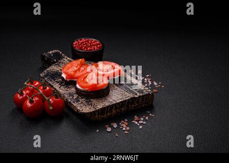 Délicieuse aubergine coupée en cercles grillée et cuite avec de la mayonnaise et des tomates sur un fond de béton foncé Banque D'Images