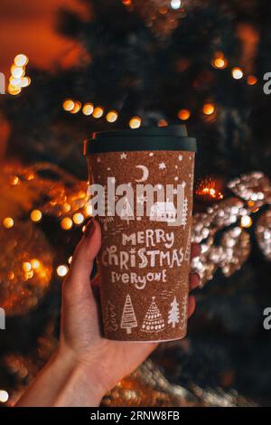 Main féminine tenant une tasse de café ou de thé avec un design du nouvel an et de Noël. Détails des vacances d'hiver, carte postale verticale Banque D'Images