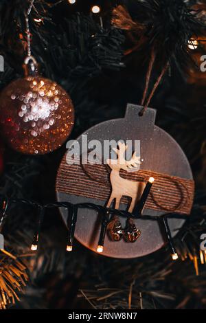 Détails en bois de Noël avec figurine de cerf accrochée sur le sapin de Noël. Détails magiques avec lumières de guirlande bokeh dorées sur fond. Banque D'Images