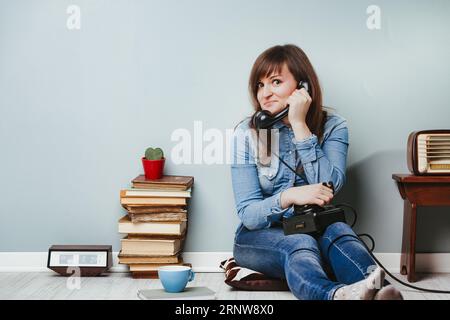 Entouré d'objets vintage, le visage d'une femme reflète l'étonnement des commérages via son vieux téléphone. La scène dépeint des contes et des mystères dans une fille à la maison Banque D'Images