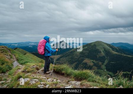 Jeune femme Backpacker habillé costume de pluie bleu avec bâtons de suivi avec sac à dos profitant de la chaîne de montagnes slovaque Mala Fatra. Concept de style de vie actif Banque D'Images