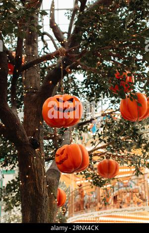 Citrouille orange avec un visage d'Halloween effrayant accroché à un arbre avec des guirlandes scintillantes. Concept de fête d'Halloween Banque D'Images