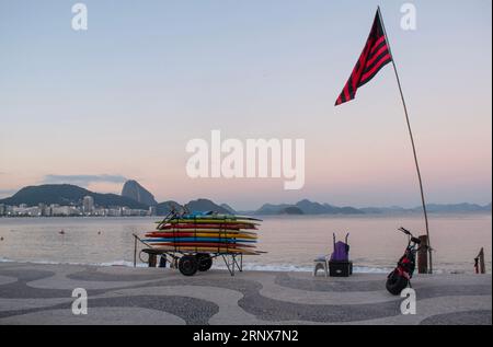 Rio de Janeiro, Brésil : planches de surf empilées sur une voiturette au coucher du soleil sur la plage d'Ipanema avec le trottoir graphique emblématique le long de l'Avenida Atlantica Banque D'Images