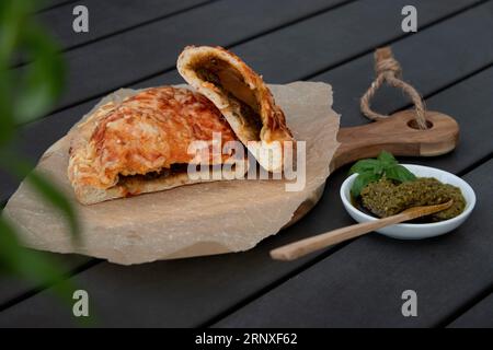 Pizza calzone découpée avec sauce tomate, pesto vert et fromage sur assiette en bois Banque D'Images