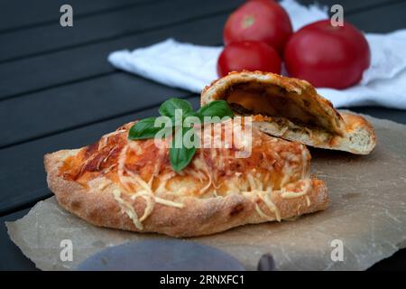 Pizza calzone découpée avec sauce tomate, pesto vert et fromage sur assiette en bois Banque D'Images