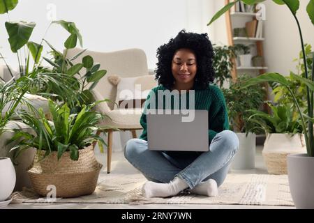 Atmosphère relaxante. Femme avec ordinateur portable entouré de plantes d'intérieur en pot dans la chambre Banque D'Images