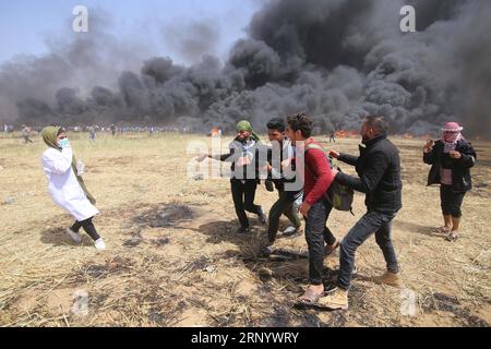 (180406) -- GAZA, 6 avril 2018 -- des manifestants palestiniens transportent un homme blessé lors d'affrontements à la frontière Gaza-Israël, à l'est de la ville de Gaza, le 6 avril 2018. Des centaines de manifestants palestiniens ont commencé vendredi à mettre le feu à des dizaines de pneus de voiture près de la frontière entre l'est de la bande de Gaza et Israël dans le but de faire un bouclier de fumée noire pour se protéger des tirs des soldats israéliens. zf) MIDEAST-GAZA-AFFRONTEMENTS KhaledxOmar PUBLICATIONxNOTxINxCHN Banque D'Images