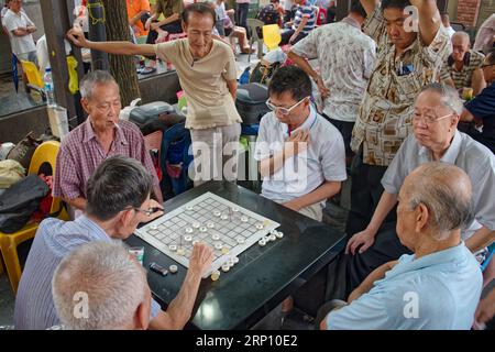 Des hommes chinois âgés et retraités de souche à Kreta Ayer Square, Chinatown, Singapour, jouant une variante chinoise des échecs, observés par des spectateurs curieux Banque D'Images