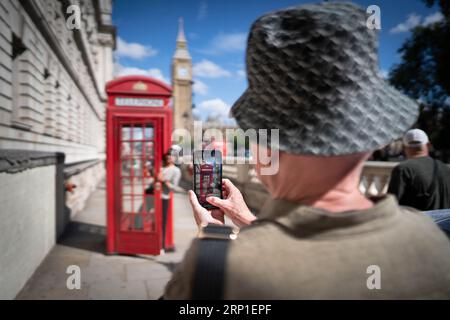 Les touristes et les visiteurs de Londres se font prendre en photo à l'intérieur d'une cabine téléphonique rouge sur Parliament Square à Westminster, alors que la popularité des célèbres stands perdure à l'ère des médias sociaux alors qu'ils approchent de leur 100e anniversaire. La célèbre boîte téléphonique rouge a été conçue par l'architecte Sir Giles Gilbert Scott pour un concours en 1924. Date de la photo : mardi 15 août 2023. Banque D'Images