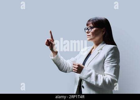 Femme d'affaires touchant avec le doigt sur l'écran virtuel, fond gris Banque D'Images