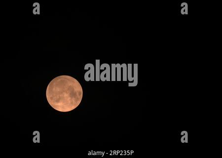 Lune rouge, en bas à gauche dans un cadre horizontal. La lune super bleue du 30 au 31 août a été largement photographiée dans le monde entier. Dans le sud de l'Angleterre, j'étais limité par mon emplacement dans une zone bâtie, dans les photos que je pouvais prendre. La lune n'était pas visible à mon emplacement jusqu'à environ 2200 heures le 30 août. À 0100 heures le 31, le ciel s'est couvert de nuages et a ainsi terminé une soirée frustrante car le temps optimal d'observation de la lune sur la côte sud de l'Angleterre, était de 0235 heures. La prochaine lune de ce genre sera en 2037. Banque D'Images