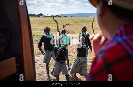 MAASAI MARA -- des enfants saluent le conservateur chinois de la faune Zhuo Qiang (à droite) alors qu'il passe à Maasai Mara, Kenya, le 6 juillet 2018. Le fondateur et président du Fonds de conservation Mara (MCF) Zhuo Qiang, un Chinois de 45 ans, a été le pionnier de projets de conservation de la faune et de la flore remarquables dans l'écosystème mondialement connu du Maasai Mara. OL Kinyei fait partie des conservatoires bénéficiant de ses activités. Autour d'elle, il a construit trois boas à l'épreuve du lion empêchant le conflit avec la faune sauvage avec les communautés adjacentes. Il a été officiellement adopté en tant que fils du groupe de conservation Maasai s OL Kinyei en 2015, en raison de Banque D'Images