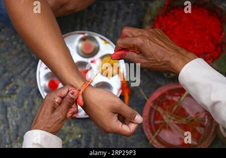 (180826) -- KATMANDOU, 26 août 2018 -- Un prêtre attache un fil sacré à un homme pendant le festival Janai Purnima au temple Pashupatinath à Katmandou, Népal, le 26 août 2018. Au cours de ce festival, les hindous prennent un bain sacré et effectuent le changement annuel du Janai, un fil de coton sacré porté autour de leur poitrine ou attaché au poignet, dans la conviction qu'il les protégera et les purifiera.) (dtf) NÉPAL-KATMANDOU-JANAI PURNIMA-FESTIVAL sunilxsharma PUBLICATIONxNOTxINxCHN Banque D'Images