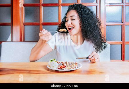 Belle fille mangeant de la crêpe au chocolat et de la crème glacée avec une fourchette. Femme affamée assise mangeant de la crêpe au chocolat et de la crème glacée Banque D'Images