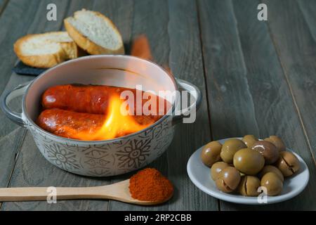 Chorizo grillé, chorizo al infierno, dans un pot en argile avec du pain, des olives et du paprika, un plat typique de la cuisine espagnole Banque D'Images