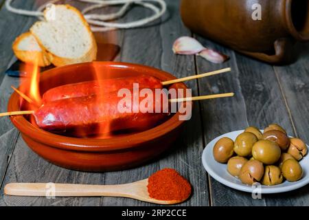 Chorizo grillé, chorizo al infierno, dans un pot en argile avec du pain, des olives et du paprika, un plat typique de la cuisine espagnole Banque D'Images