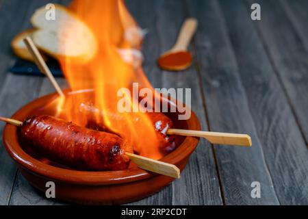 Chorizo grillé, chorizo al infierno, dans un pot en argile avec du pain, des olives et du paprika, un plat typique de la cuisine espagnole Banque D'Images