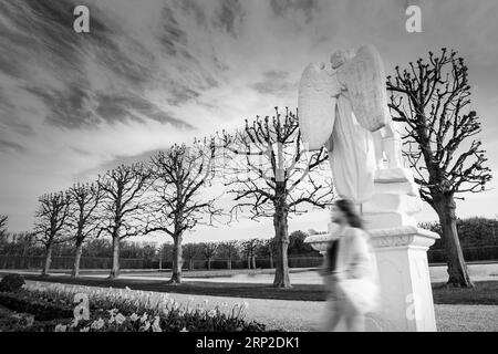 Fantôme dans le parc. Photographie en noir et blanc. Une personne défocalisée sur le fond d'un ciel de mauvaise humeur et d'une sculpture d'ange. Dramatique poétique Banque D'Images