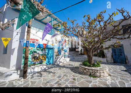 Petite place avec des maisons peintes, des arbres et des drapeaux colorés, ruelles du village Marpissa, Paros, Cyclades, Grèce Banque D'Images