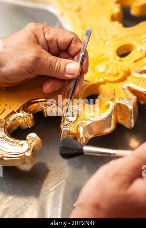 Détail d'un miroir doré à la feuille d'or, un homme pose un morceau de feuille d'or avec une pince à épiler et le caresse avec un pinceau Banque D'Images