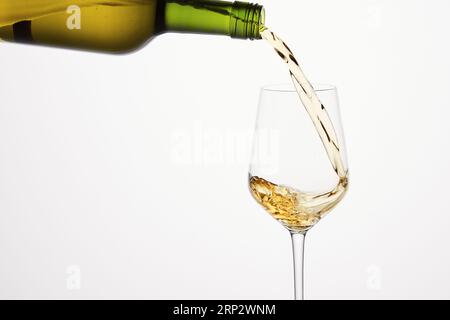 Vin blanc coulant de bouteille verte sur blanc isolé. Banque D'Images