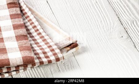 Trois serviettes de cuisine brunes à carreaux reposent sur une table de cuisine en bois blanc. Banque D'Images