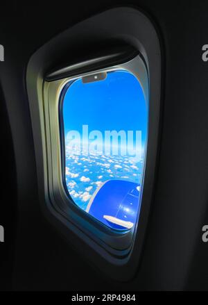 Champ emblématique de nuages gonflés vus de la fenêtre de l'avion. Un capot de moteur à réaction est en vue, fournissant le contexte. Un portail ovale vers le monde extérieur. Banque D'Images