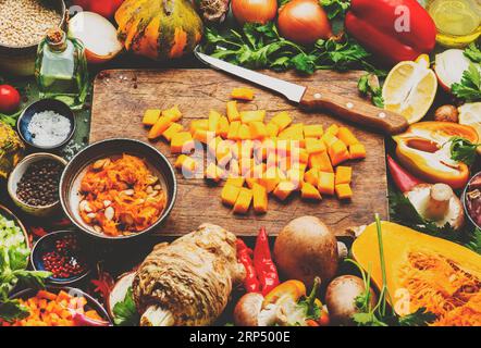 Fond alimentaire. Couteau de citrouille pelée crue en dés et légumes sur une planche à découper en bois rustique. Légumes, champignons, racines, épices - ingrédients pour v Banque D'Images