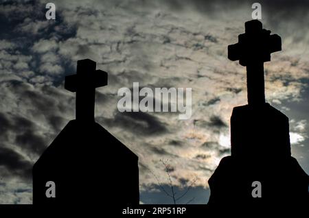 Silhouette de croix tombales dans un cimetière chrétien au coucher du soleil. Banque D'Images