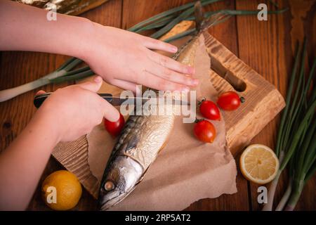 Gros plan de maquereau fumé. Mains femelles coupant le poisson avec un couteau dans la cuisine. Banque D'Images