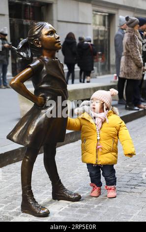 (181210) -- NEW YORK, 10 décembre 2018 -- Une fille regarde la fille sans peur dans la rue devant la Bourse de New York, aux États-Unis, le 10 décembre 2018. Fearless Girl, une célèbre statue en bronze située dans le quartier financier de New York, a été dévoilée lundi matin dans sa nouvelle maison devant la Bourse de New York (NYSE). Fearless Girl a d'abord été installée face à face avec l'emblématique statue de Charging Bull au Bowling Green Park dans le Lower Manhattan, à quelques pâtés de maisons de son emplacement actuel, à la veille de la Journée internationale de la femme en mars 2017 comme temporaire Banque D'Images