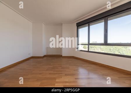 Chambre vide avec une grande fenêtre à trois vitres donnant sur un parc, parquet, aluminium gris et stores roulants Banque D'Images