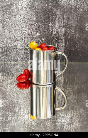 Une tasse en acier pleine de tomates cerises sur une surface réfléchissante grise Banque D'Images