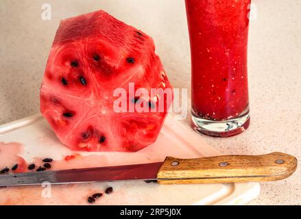 Melon tranché, couteau et mélangeur avec smoothie de melon sur le tableau de cuisine, gros plan. Banque D'Images