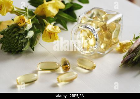 Capsules de gel d'huile d'onagre renversées d'une bouteille en verre sur une table blanche. Complément nutritionnel. Banque D'Images