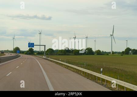 Les éoliennes se dressent le long de la route sur fond de nuages. Production d'énergie écologique verte. Banque D'Images